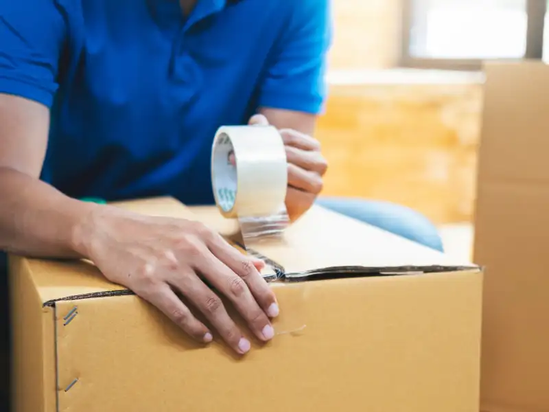 Person sealing a cardboard box with packing tape.