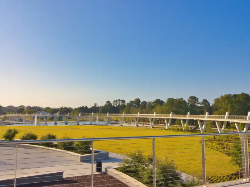 Pedestrian bridge over a bright yellow field under a clear blue sky.