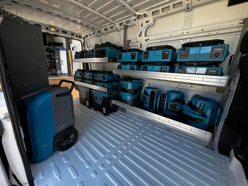 Cargo van loaded with blue power equipment and batteries on shelves.