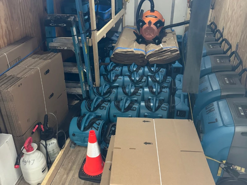 Storage room packed with stacked blue vacuum cleaners and cardboard boxes.